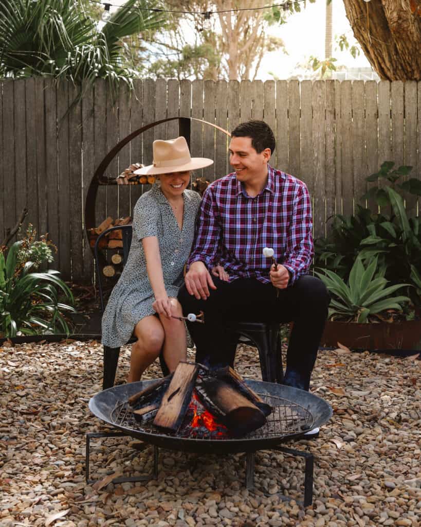 A young male and female couple cooking some marshmallows over the fire pit in the rear yard of Silvermere Coastal Retreat Culburra Beach South Coast NSW.