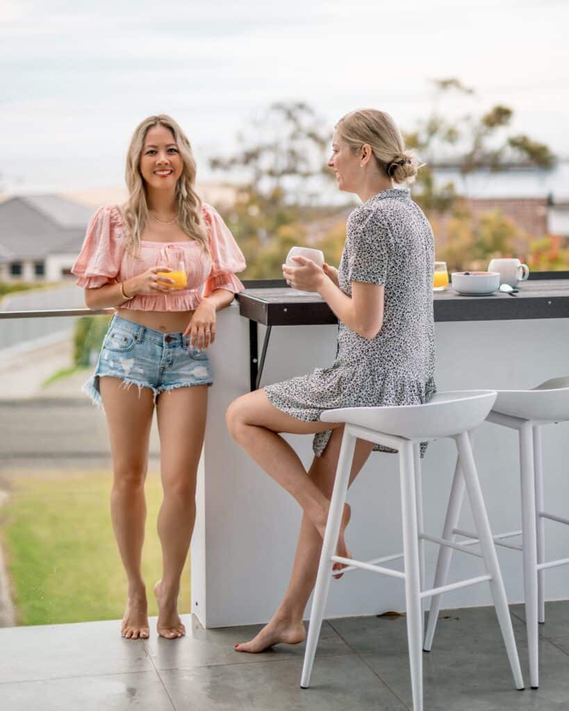 Two young females are on the upstairs balcony of Silvermere Coastal Retreat Culburra Beach South Coast NSW. They are enjoying breakfast at the breakfast bar whilst watching the view.