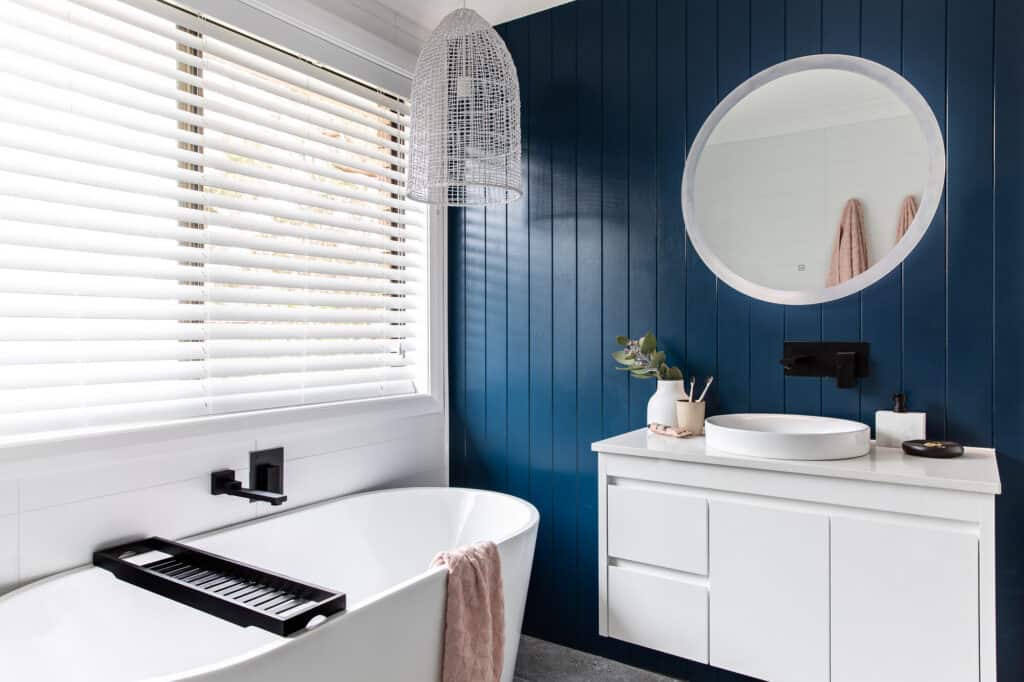 The image is a view of the bath, vanity and light up mirror on the back of a beautiful dark blue vj wall in Silvermere Coastal Retreat Culburra Beach South Coast NSW.