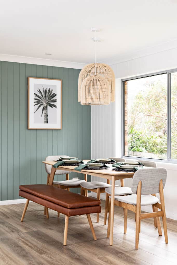 Image of upstairs dining space of Silvermere Coastal Retreat Culburra Beach South Coast NSW. In the image is a table with a brown leather bench seat, rattan pendants and a beautiful bush colour green painted on vj boards.
