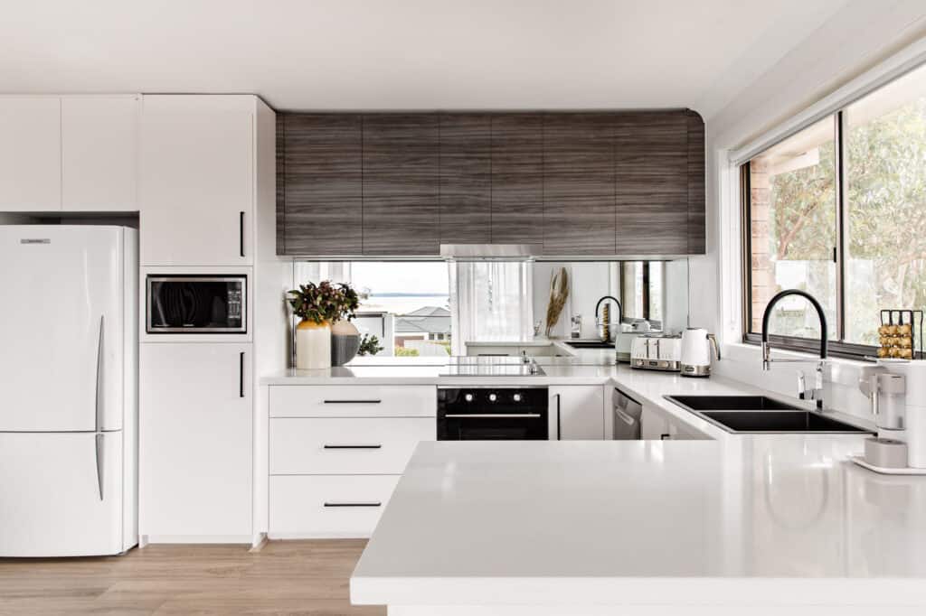 The image is of the freshly renovated white upstairs kitchen at Silvermere Coastal Retreat Culburra Beach South Coast NSW. The kitchen is fully equipped with everything a family need to use to cook, clean and make coffee.