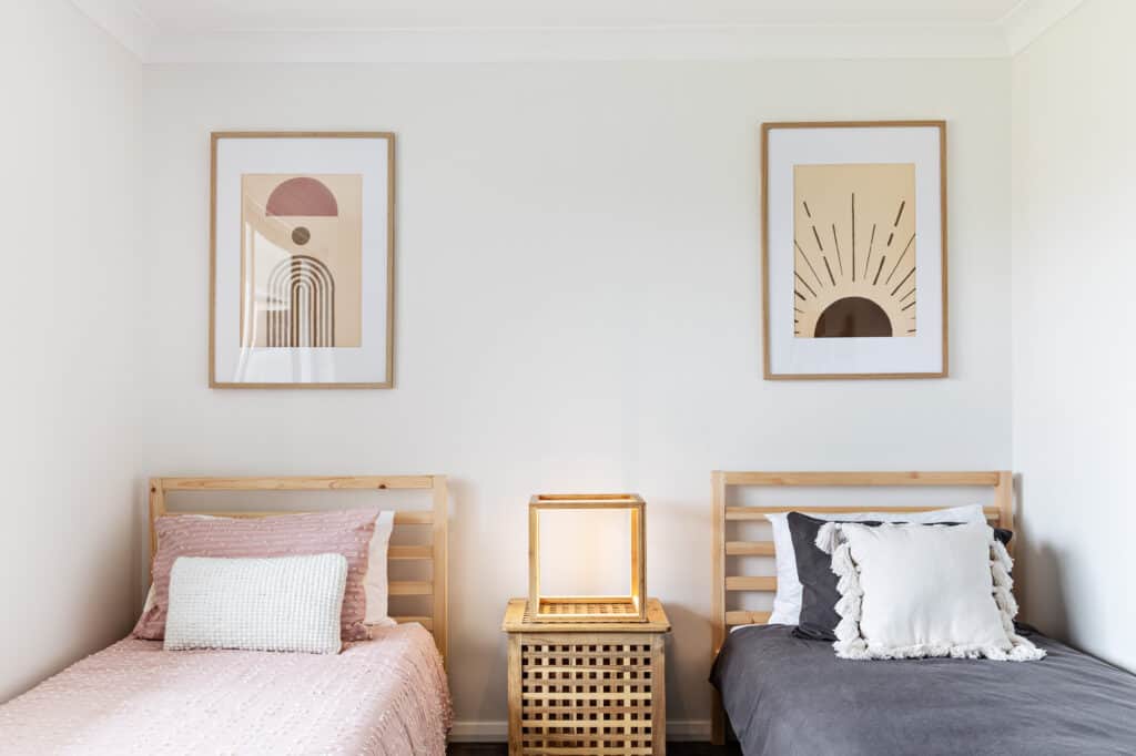 Image of the single bedroom at Silvermere Coastal Retreat Culburra Beach South Coast NSW. In the image are the 3 single beds, a wooden square lamp and two hand-painted prints.