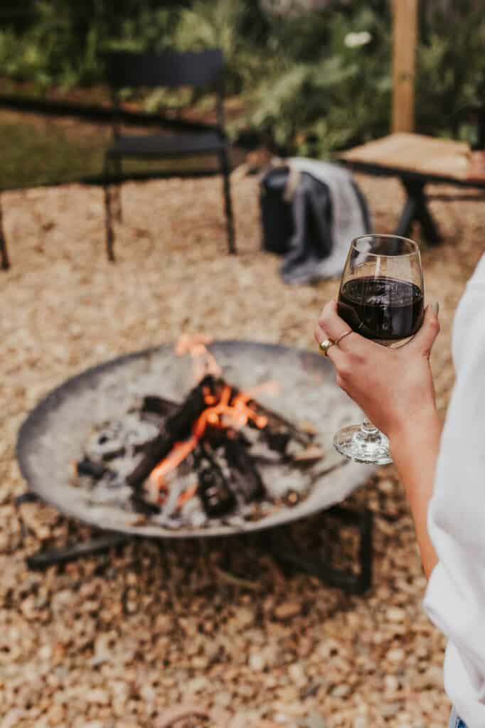 A young lady is standing by the fire pit with a red wine in hand watching the fire in the rear yard of Silvermere Coastal Retreat in Culburra Beach South Coast NSW.