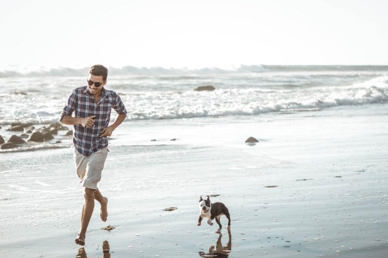 Man running down the beach with his dog chasing him Culburra Beach on South Coast NSW.